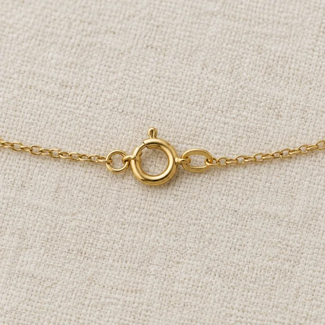 Gold necklace clasp and chain links on cream linen.