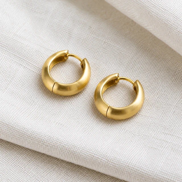 Pair of unbranded brushed-gold hoop earrings on pale linen.