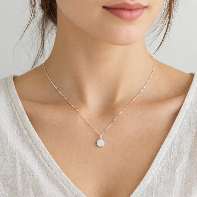 Delicate silver pendant necklace worn at the collarbone over a linen blouse.