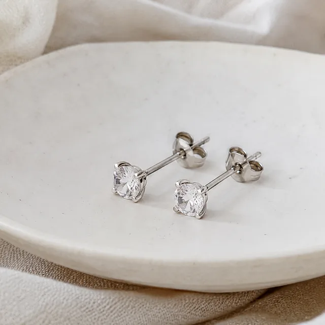 Pair of simple silver stud earrings on a pale ceramic dish.