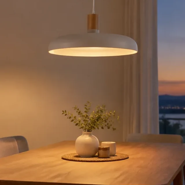 Square crop of a pendant lamp glowing above a dining table.
