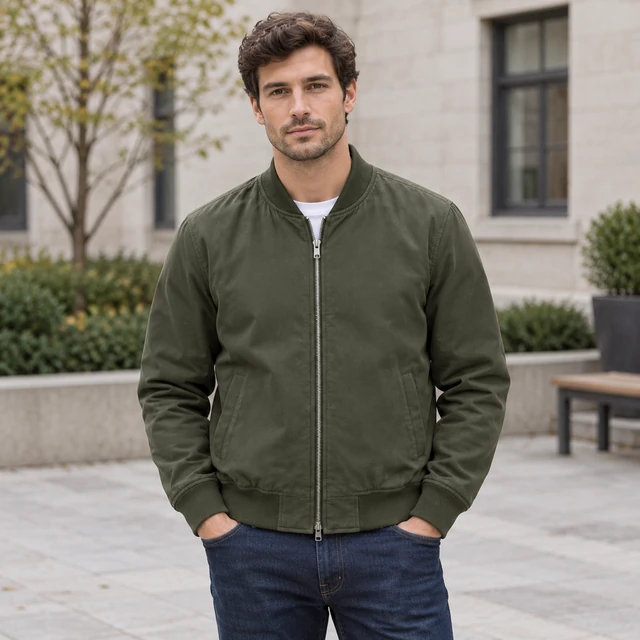 Adult model wearing a plain olive bomber jacket in a quiet city courtyard.
