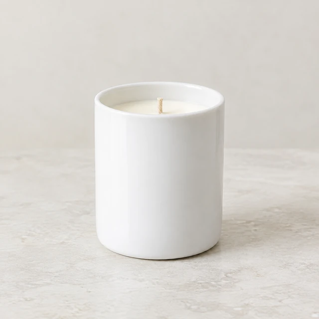 Plain white ceramic candle jar standing by itself on a neutral surface.
