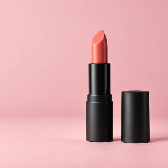 Coral lipstick in a matte black tube with its cap on a soft pink backdrop.