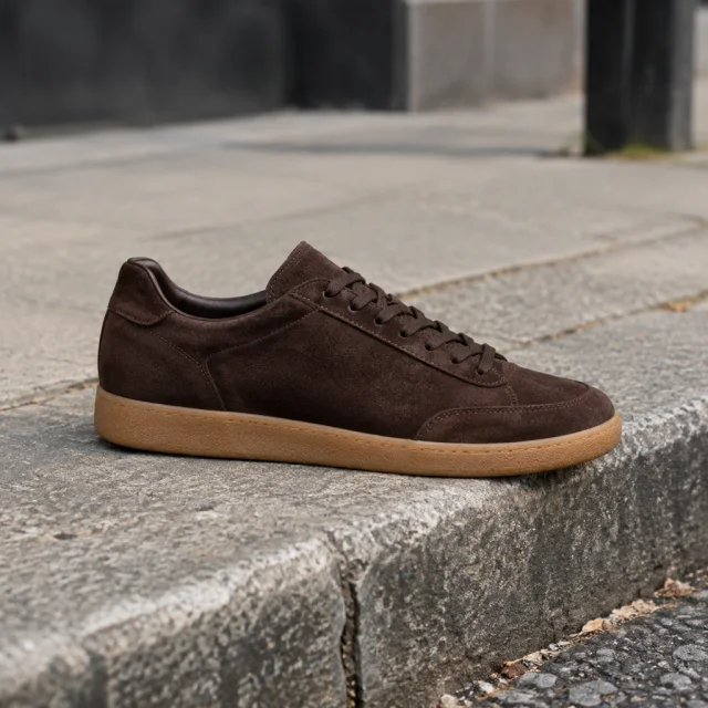 Brown suede trainer with a gum sole on a city curb.