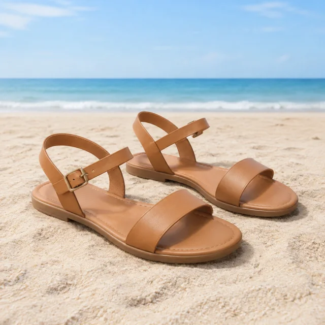 Simple summer sandals arranged on sand with open space above.