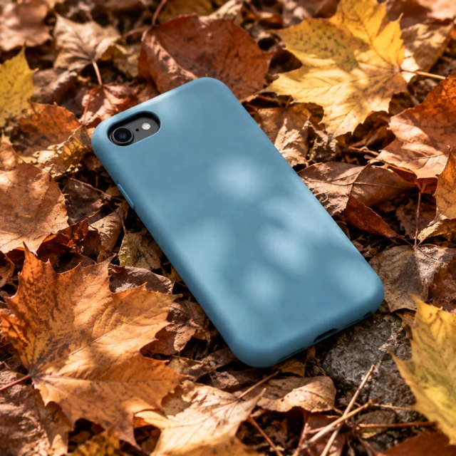 Plain sea-blue protective case with one small oval camera opening among dry autumn leaves.