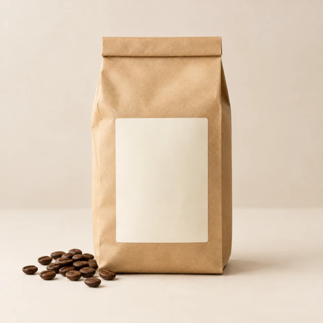 Blank kraft coffee bag with scattered beans on a pale studio surface