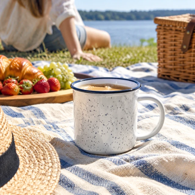 Enamel camping mug on a summer picnic blanket in bright sun.