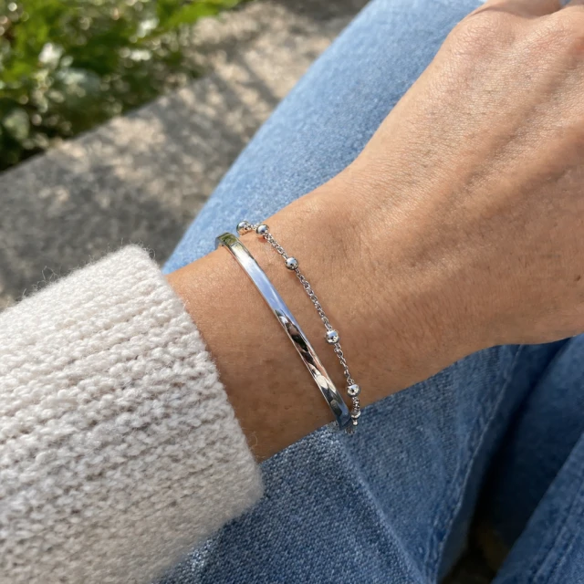 Silver bracelet stacked on a wrist in daylight.