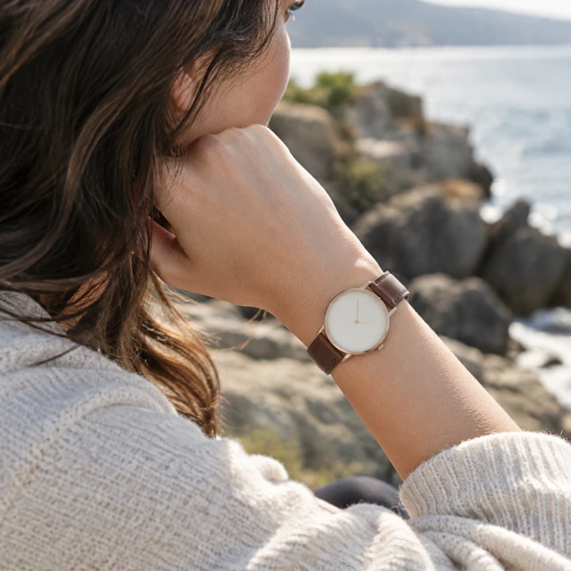 Minimal leather strap watch with a plain round dial on a wrist outdoors.