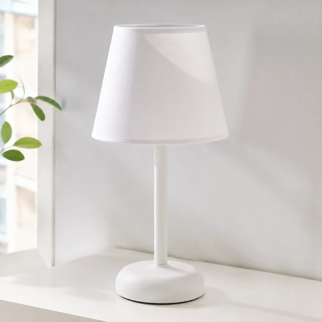 Plain white table lamp with a tapered shade on a pale tabletop.