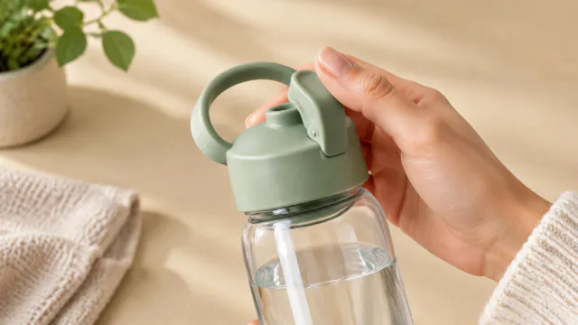 Hand holds the pale green lid of a clear water bottle beside a plant.